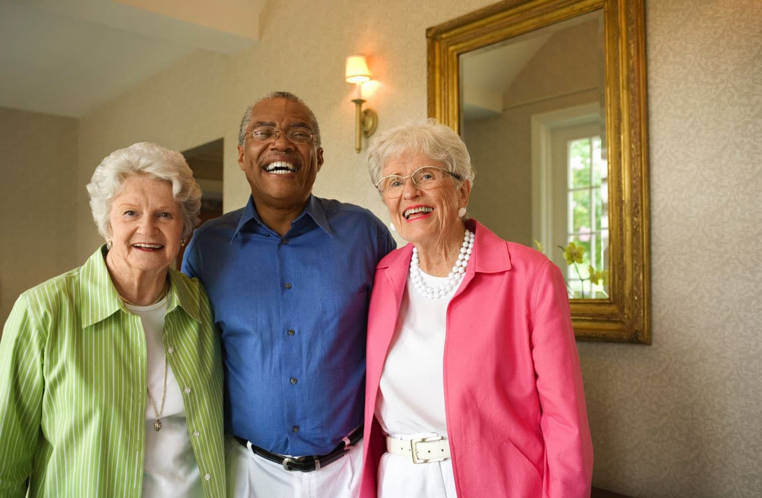 two senior women and one senior man joyfully laughing inside their senior living community they call home